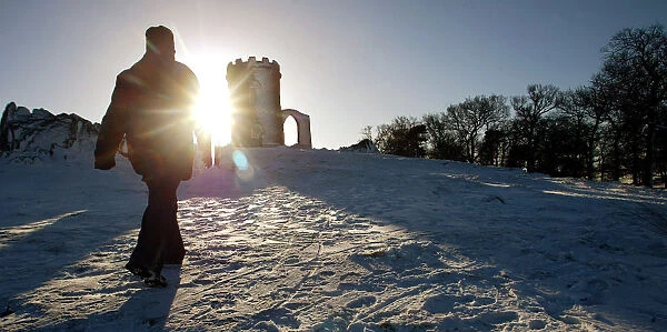 A WALKER STRIDES THROUGH SNOW TOWARDS THE OLD JOHN MEMORIAL IN BRADGATE PARK