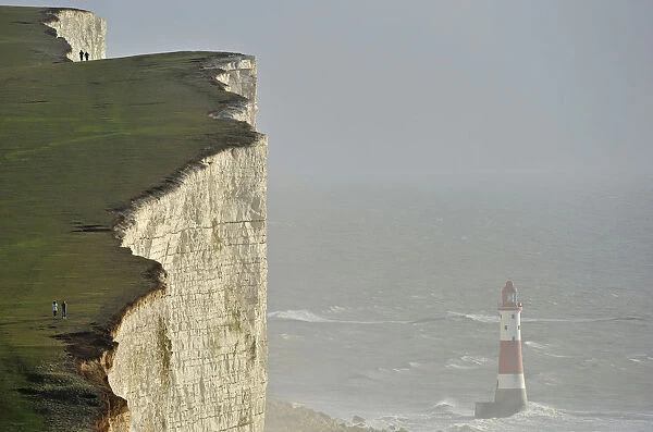 Walkers look out over Beachy Head lighthouse and heavy seas in the English Channel
