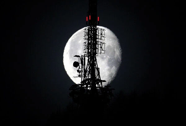 The waning gibbous moon shines behind a telecommunications tower in the Swiss mountain