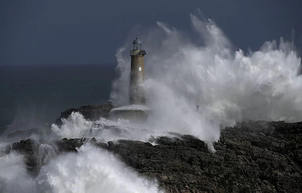 Waves crash on the lighthouse of La Isla del Mouro in the port town of Santander