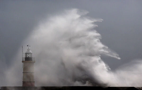 Waves crash against the lighthouse and sea wall during high winds
