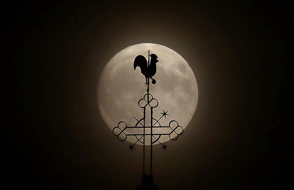 The weathercock of the church of St. Peter and Paul is seen in front of a moon on the eve