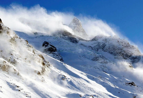Wind blows snow off the top of a mountain in Saint-Pancrace as winter weather bringing