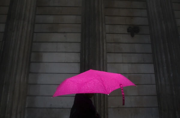 A woman carries an umbrella during a rain shower as she walks past the Bank of England