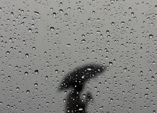 A woman carrying an umbrella is silhouetted from behind a window covered with rain drops