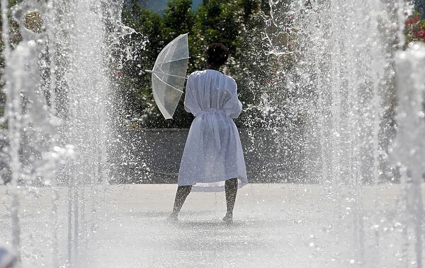 A woman cools off in water fountains in a park as hot summer temperatures hit Paris