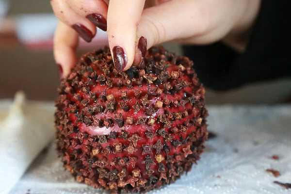 A woman decorates an apple with carnation seeds, which is a popular traditional gift