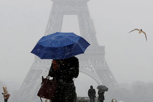 A woman holding an umbrella walks as snowfall near the Eiffel Tower in Paris
