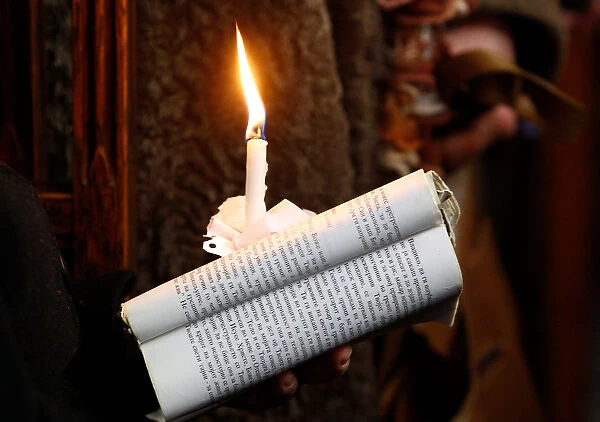 A woman holds a candle and the Bible during the Orthodox Christmas mass at the St