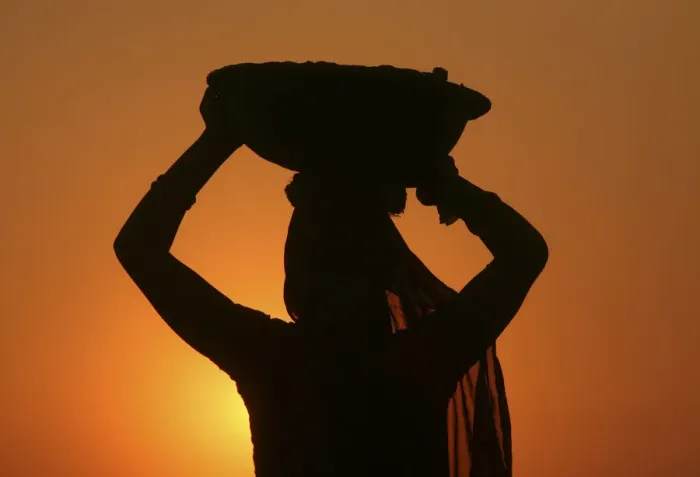 Framed Print : A woman labourer carrying cement is silhouetted against the setting sun at the site of a Framed Print : A woman labourer carrying cement is silhouetted against the setting sun at the site of a