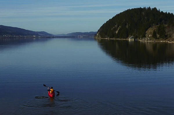 A woman paddles her kayak on the Lac de Joux on a sunny morning in Le Pont