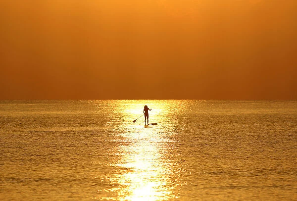 A woman paddles on a stand-up board during sunrise in a beach in Larnaca