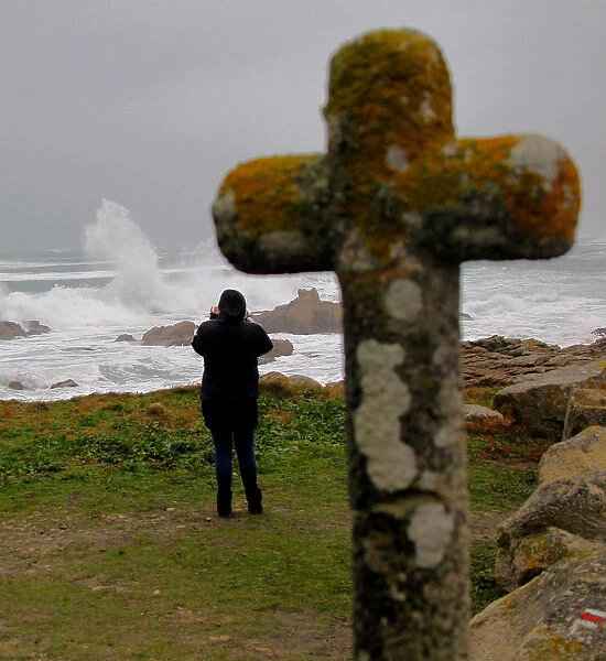 A woman photographs waves breaking on the Brittany coast after storm Eleanor hit