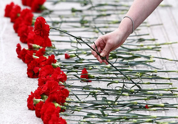 A woman places a red carnation flower on the ground by a pool outside the Scottish