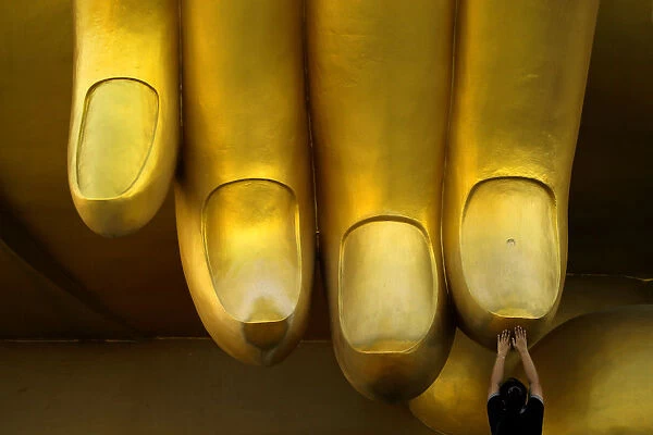 A woman prays while touching the fingers of a Buddha statue during the annual Makha Bucha