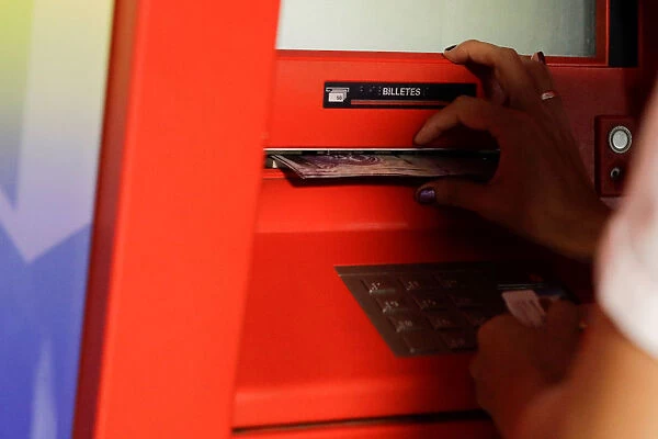 A woman receives Bolivar notes from an ATM in Caracas