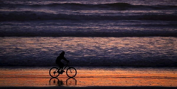 A woman rides her bicycle at sunset on a beach in La Serena