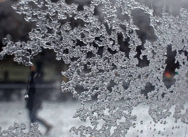 A woman is seen walking in the background through a sheet of glass, on which ice particles