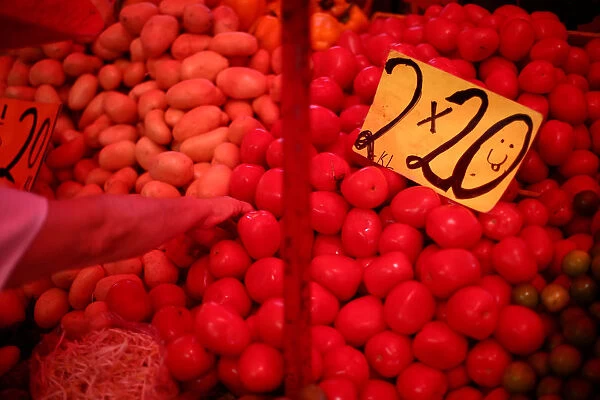 A woman selects vegetables next to sign that displayed the price of tomatoes at a store