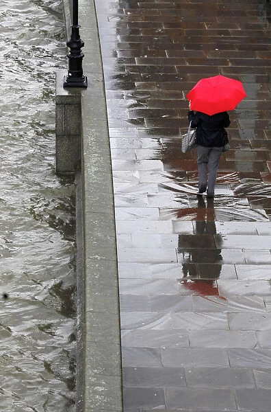 A woman shelters under her umbrella as she walks alongside the River Thames during