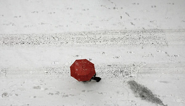 A woman shields herself under an umbrella as she walks during a heavy snowfall in