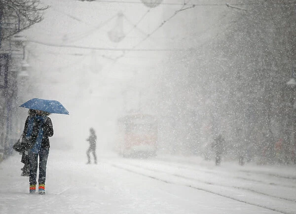 A woman shields herself under an umbrella as she walks during a heavy snowfall in