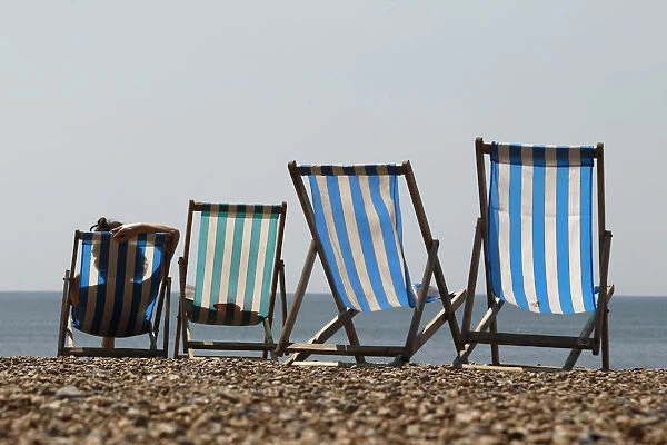 A woman sunbathes in a deckchair by the sea on a sunny day on Brighton Beach in southern