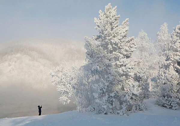 A woman takes pictures on a bank of the Yenisei River covered with snow and hoarfrost
