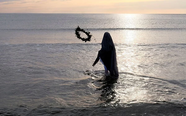 A woman throws a wreath into the water during a procession of the Santisimo Cristo del
