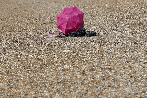 A woman with an umbrella sits by the sea on a sunny day on Brighton Beach in southern