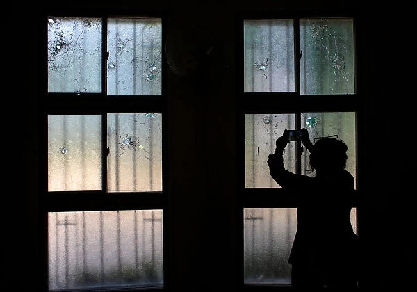 A woman uses her mobile phone to take pictures of bullet holes in windows damaged during