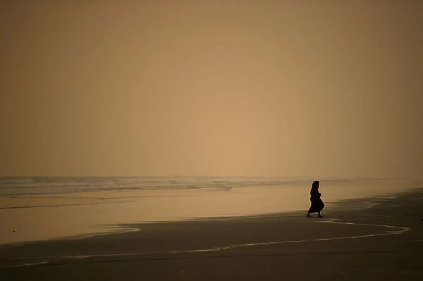 A woman walks along the beach at sunset in Coxs Bazar