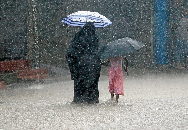 A woman walks with a girl along a flooded road in the heavy rains in Malwana