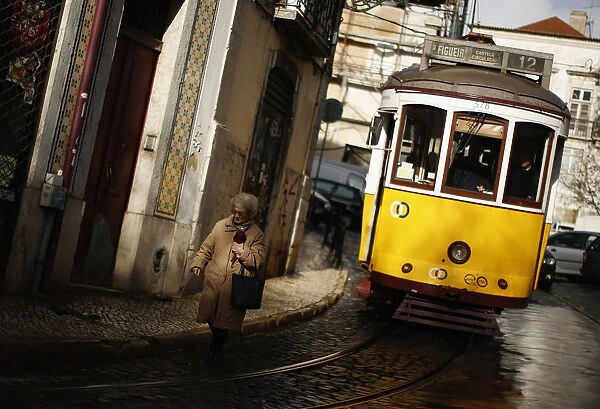 A woman walks near a tram at the Alfama neighborhood in Lisbon