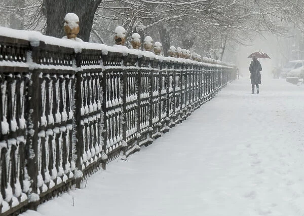 A woman walks along a park fence during a snowfall in Almaty