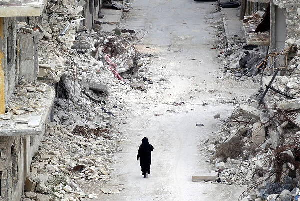 A woman walks past damaged buildings in the rebel-controlled area of Maaret al-Numan town