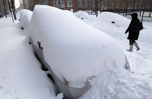 A woman walks past a row of cars buried in the snow in Hoboken