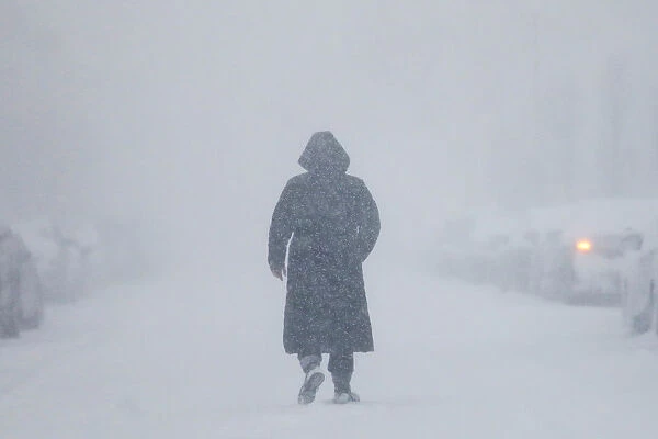 A woman walks down the street during a blizzard in Long Beach