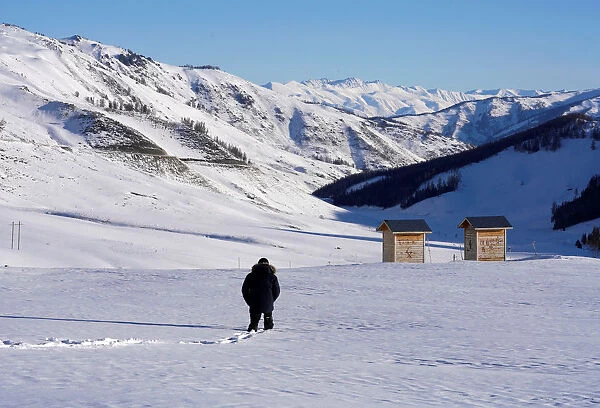 A woman walks toward a toilet among mountains covered with snow in Hemu of Altay