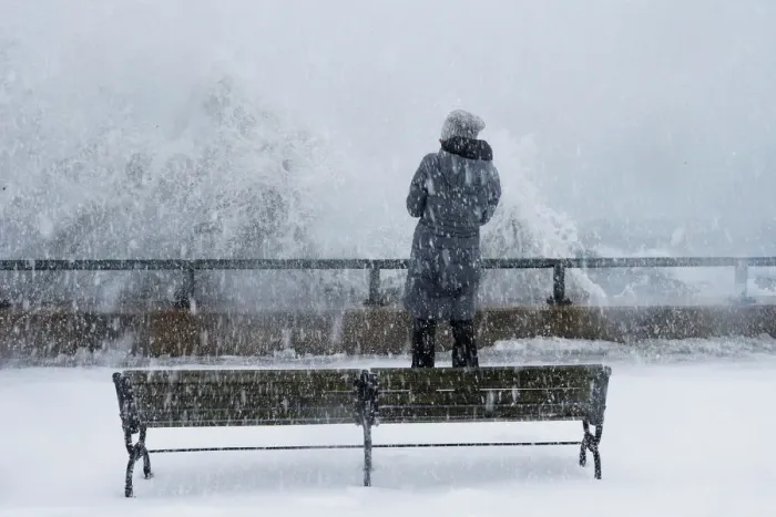 Framed Print : A woman watches as ocean waves overtop the seawall during a winter snow storm in