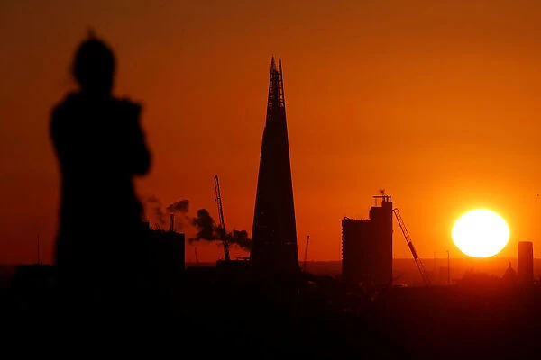 A woman watches the sun rise behind the Shard from Primrose hill in London