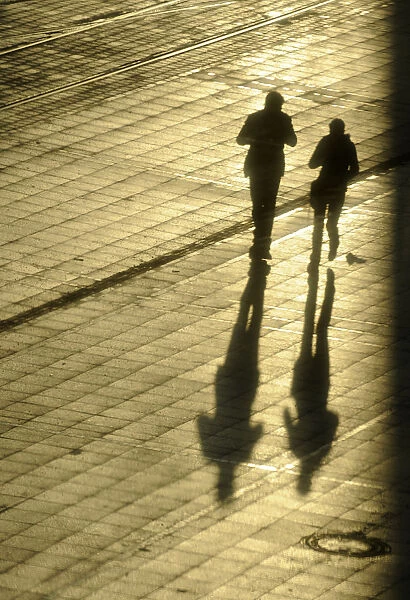 Women cast their shadows in the setting sun as they walk past the headquarters of
