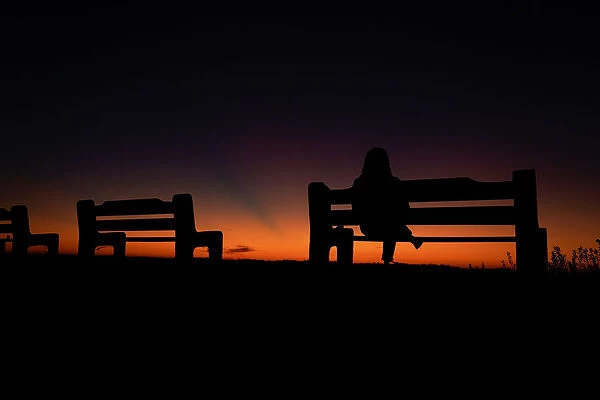 A women sits alone on a park bench watching the sky after sun set in Encinitas