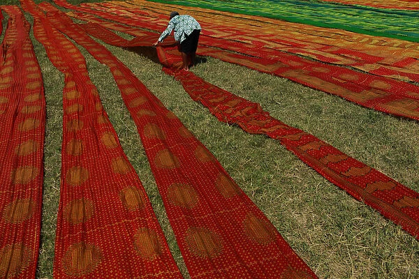 A worker lays batik cloth out on the grass to dry in Solo