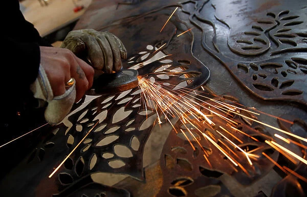 A worker uses an angle grinder on a piece of metal at a steel workshop in Marseille