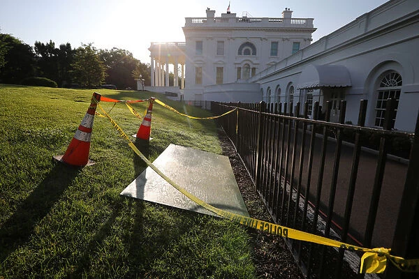 Yellow caution tape and cones are seen around a sinkhole next to the entrance of the