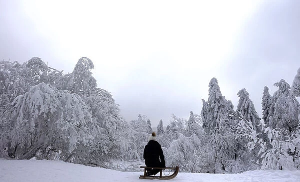 A young girl sits on her sledge on top of the Feldberg mountain during a winter day