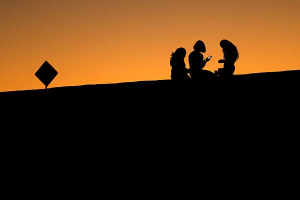Young girls look at their phones as they sit on a hillside after sun set in El Paso