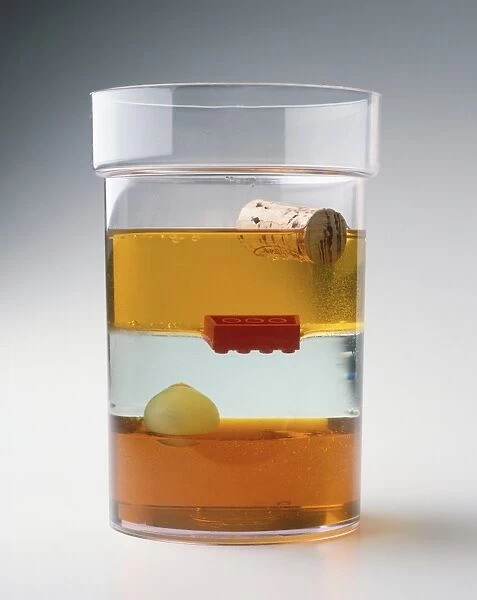 Glass containing layers of fluid of different densities, including syrup, water, oil, and objects floating on layers