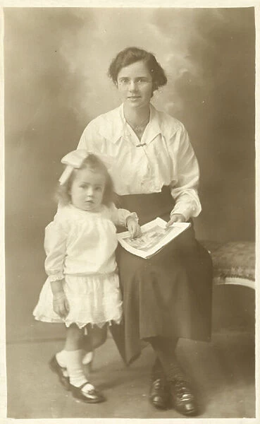 Pretty girl, mother or governess, showing photos to young child (b  /  w photo)